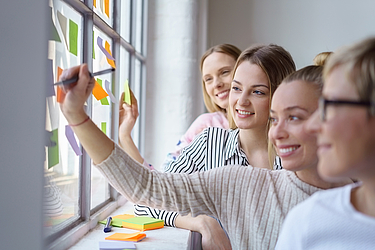 4 Frauen stehen lächelnd vor einem Fenster und beschriften dort Post-its. ©iStock/stockfour