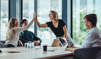 Zwei Frauen und zwei Männer befinden sich während einer Besprechung. Die beiden Frauen klatschen ab ©iStock/jacoblund